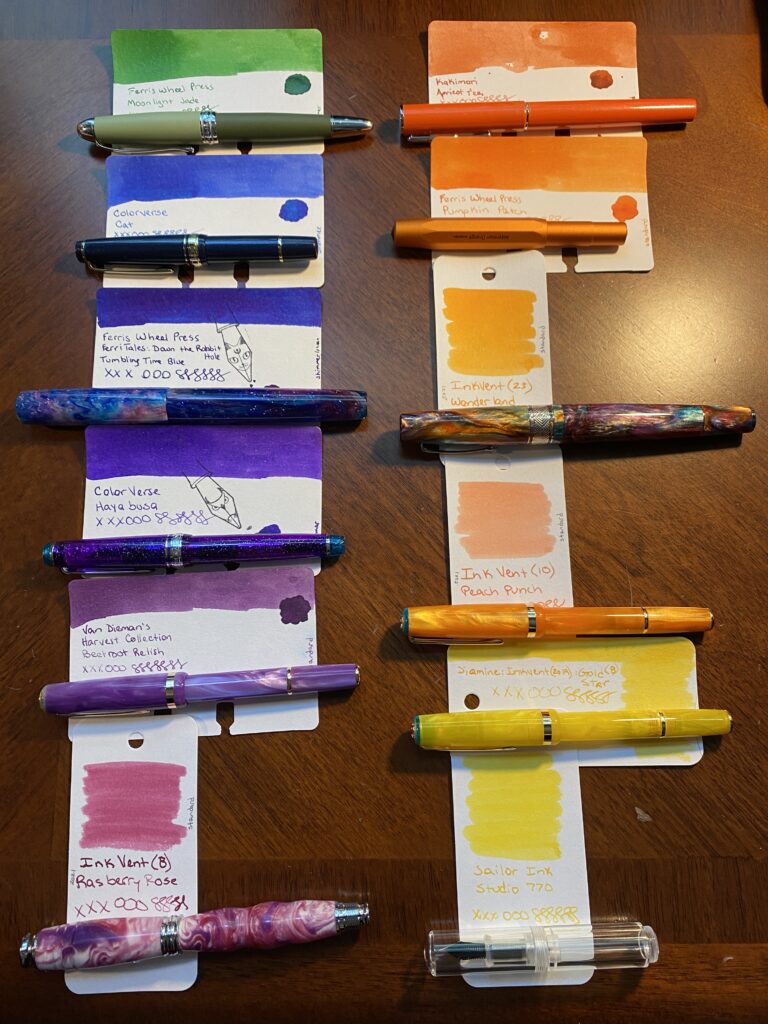 There are two columns of pens and ink sample cards laid out side by side. The left column starts with a dark green, then a blue, then a darker blue/purple, then purple, then a slightly lighter purple, and last a rose magenta color. The right side colum starts with a darker orange, then a slightly lighter orange, and then another slightly lighter orange, then a peach, then a darker yellow, and last a lighter yellow. The names of the pens and the inks are listed below the photo. 