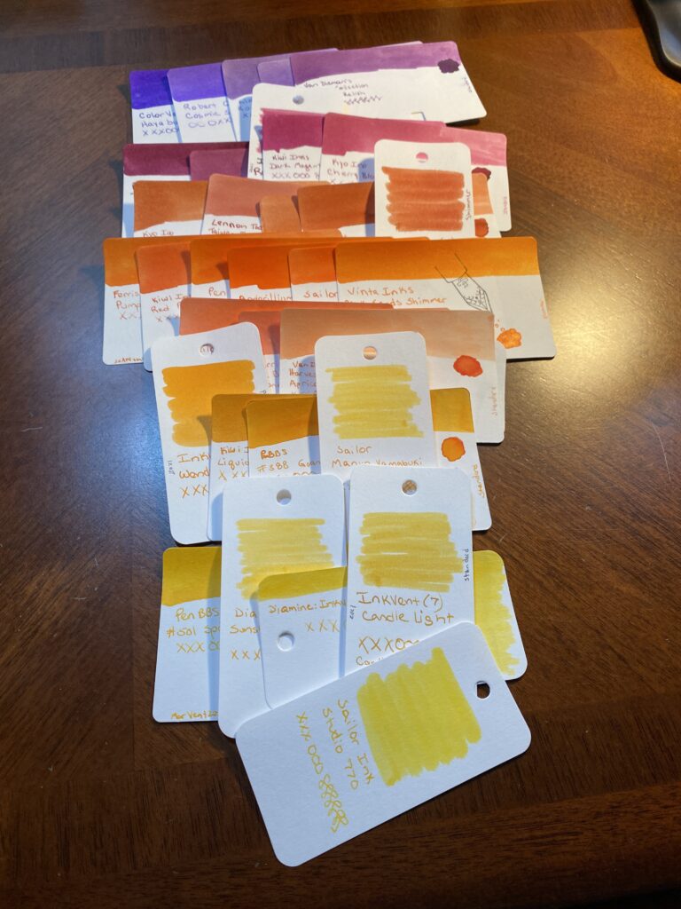 Line of 5 purple cards, underneath that is 5 magenta cards, below that is 5 darker orange cards, then 6 medium/bright oranges, under those are 3 peach colored oranges, next is 4 orange/yellows, then 5 brighter yellows. These rows are all overlapping the ones above and below and beside each other. 