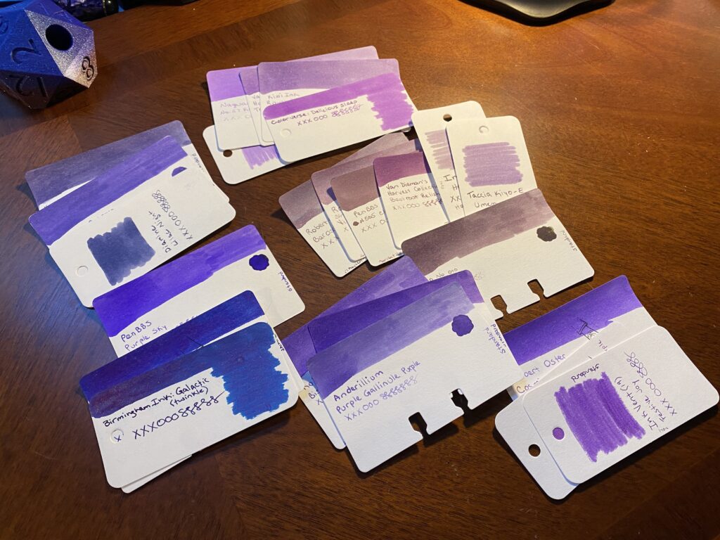 The larger pile of purple sample cards have been separated out into smaller piles, grouped by tone. The purples range from a blue/purple, dark reddish purples, dark blueish, to lighter reddish and blueish purples. 