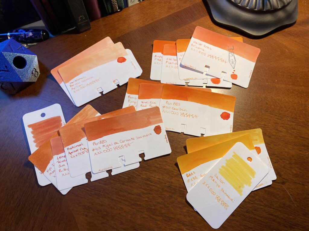 The larger pile of orangeish sample cards have been separated out into smaller piles, grouped by tone. There are some dark oranges, ones that are more peach colored, some with more red in them, some more variable, and some more yellowish. 
