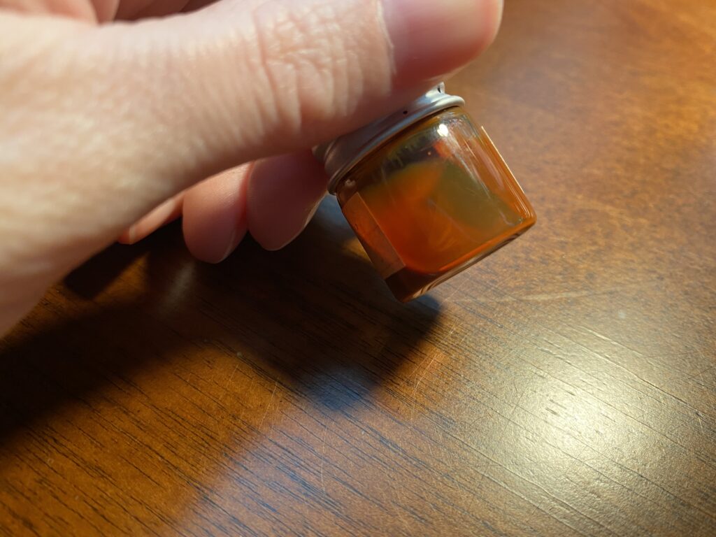 A hand holding a very small clear glass bottle with a silver cap with an opaque orange liquid inside.