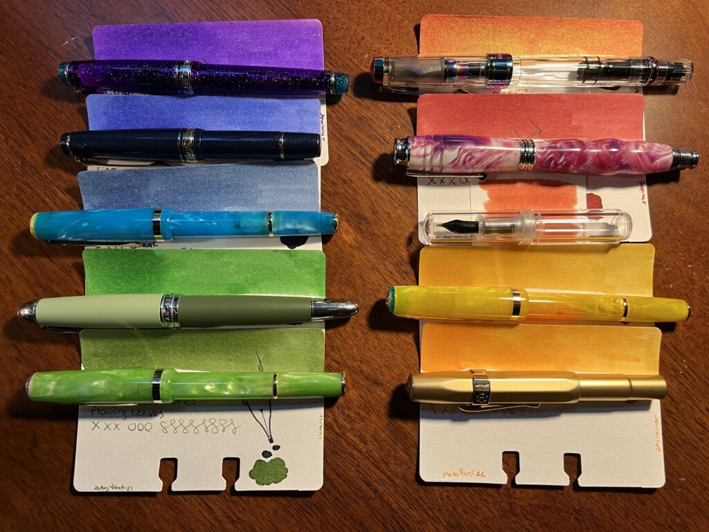 Ten pens and ten sample cards in two columns. Each pen is laid on top of a sample card just below the swatch of color at the top of the card. 