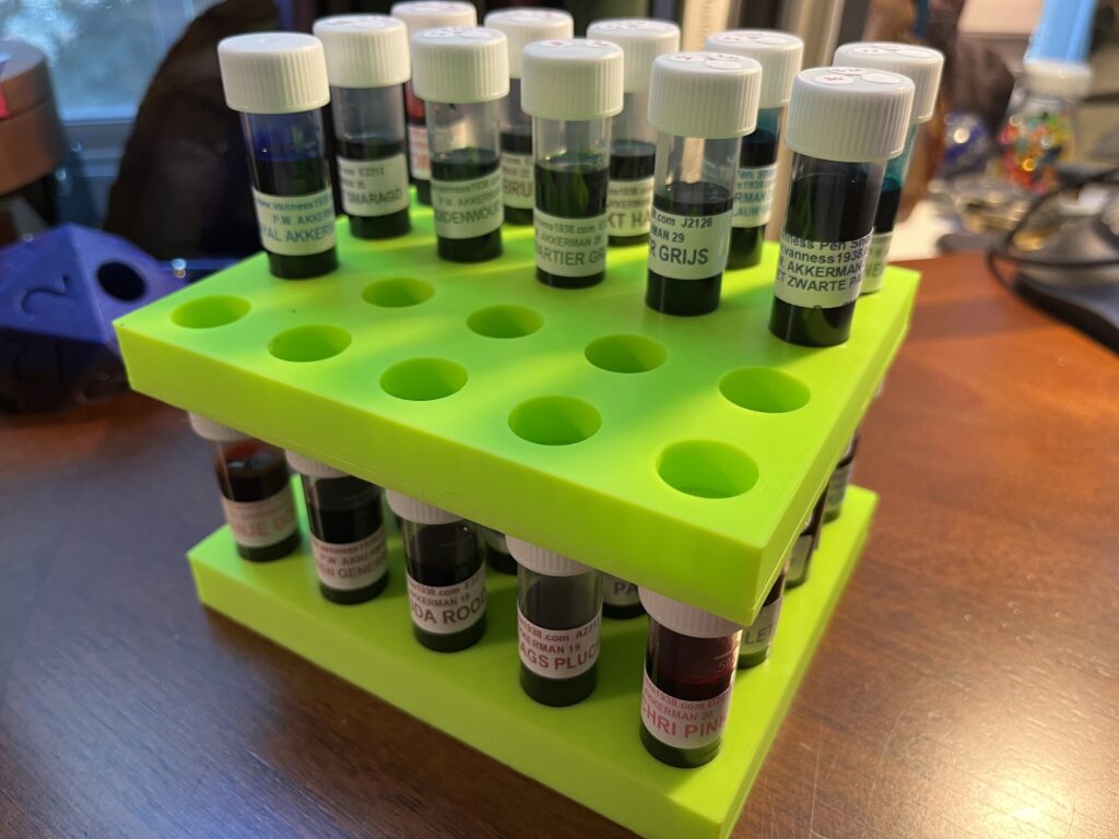 Two lime green trays, the bottom one holds 20 ink sample vials, the top one is set on top of those vial caps, and holds 11 more vials. Each vial has a label which says what the ink is. 