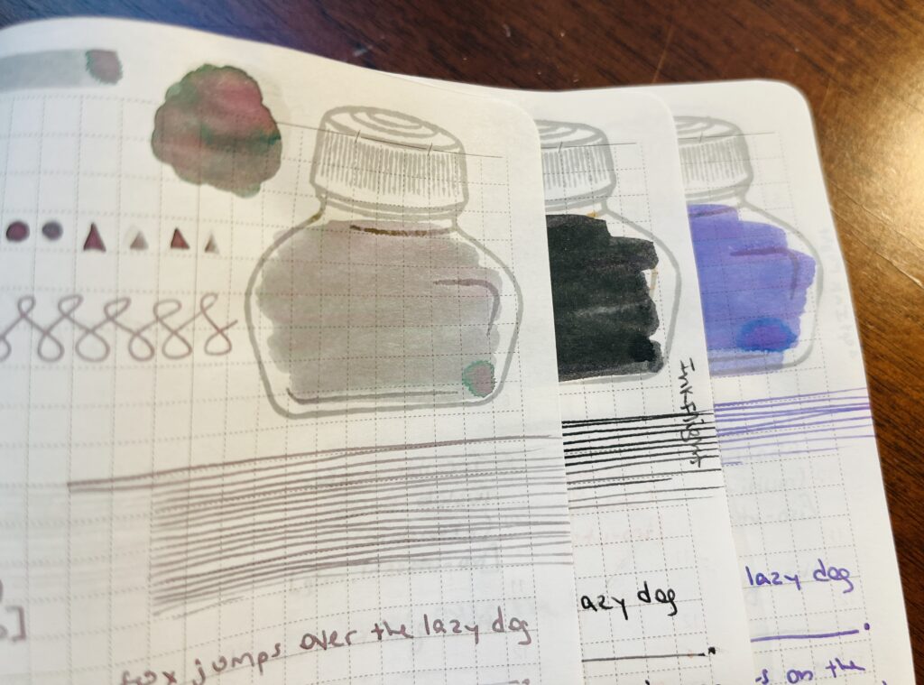 3 overlapping pages, a grey, a dark green, and a blueish purple. The page with the grey ink is the most visible. There is an ink stamp colored in with grey ink. To the left of that is a pool of the same ink, but greens and pinks can be seen. There are triangle and circle shapes, continuous s shapes, and straight lines. The only text that can be seen read “fox jumps over the lazy dog.”