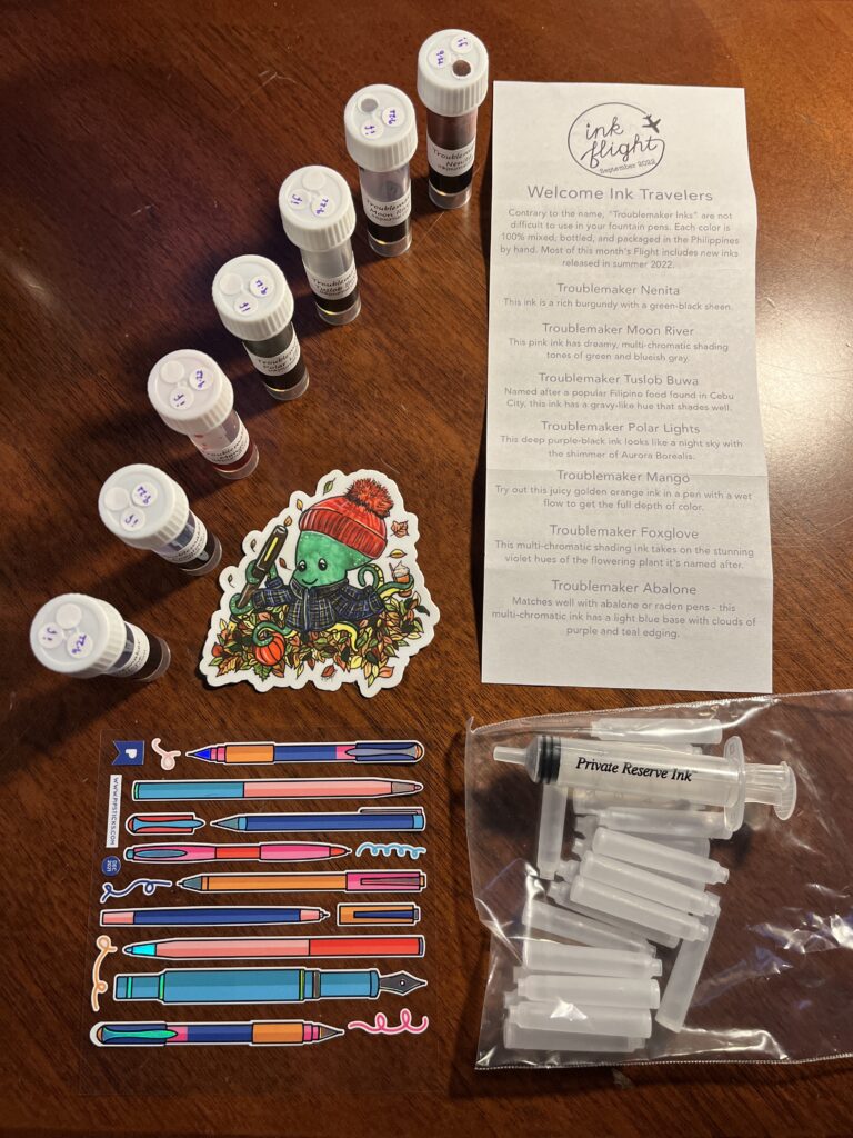 7 ink vials frame a sticker of an octopus in a knit hat and flannel coat, holding a pen, pumpkin, and a cup. There is a long narrow piece of paper listing all of the inks. Below that is a clear plastic bag with empty ink cartridges and a syringe labeled Private Reserve Ink. In the bottom left hand corner is a sheet of stickers that look like different kinds of pens. 