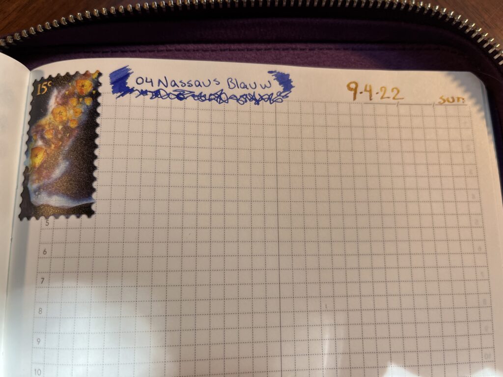 A notebook page - there is a sticker applied to the top left corner, it looks like a sample that has floating lantern art. To the right of the sticker is text reading “04 Nassaus Blauw” with scribbled marks to the left and underneath and the right side. In gold ink in the top right hand corner the text reads “9.4.22 Sun”