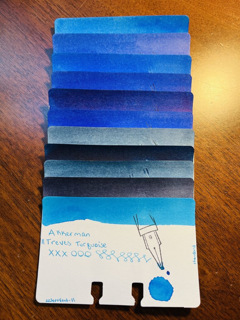 11 sample cards of different blue stacked on top of each other, only the color band at the top is visible on 10 of the cards. The last one is fully visible. It reads “Akkerman 11 Treves Turquoise, xxxooosssssss, 22SeptVent-11, standard” There is a stamp of a nib with a B on it, and a pool of the color used on the card. 