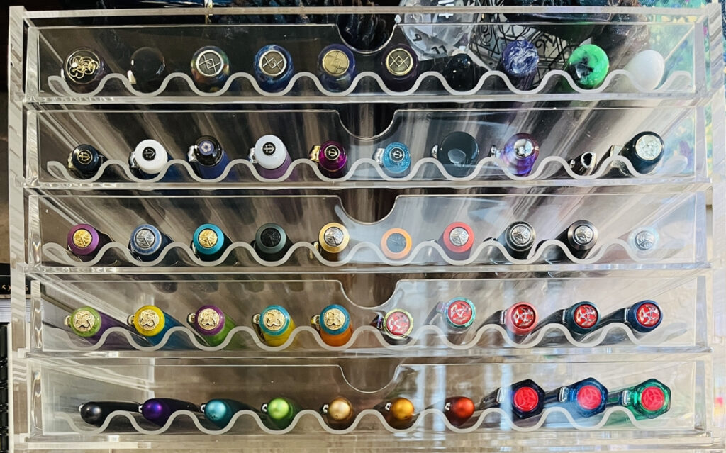 5 clear cryptic drawers, with curved clear acrylic drawer inserts, each row has 10 pens, the bottom two rows look like rainbows, the rest of the rows are various colors. 