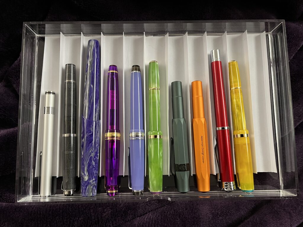 Top down view of various pens, the edge of paper dividing each pen look like a uniform height, same height as the drawer, and it looks much neater. 