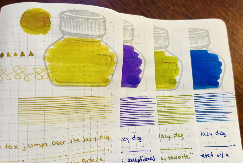 The edges of four pages in a journal. Each page has samples of a single ink, a tan gold, a bright purple, grass green, dark blue. Only the edges of the ink bottle mark and the lines drawn are visible on three of the pages. The top page you can see the geometric shapes, ink pool, ink bottle color in, straight lines, the end of the phrase “the quick brown fox jumps over the last dog” then a page separator of a straight line followed by a dot repeated, and then thoughts on the ink.