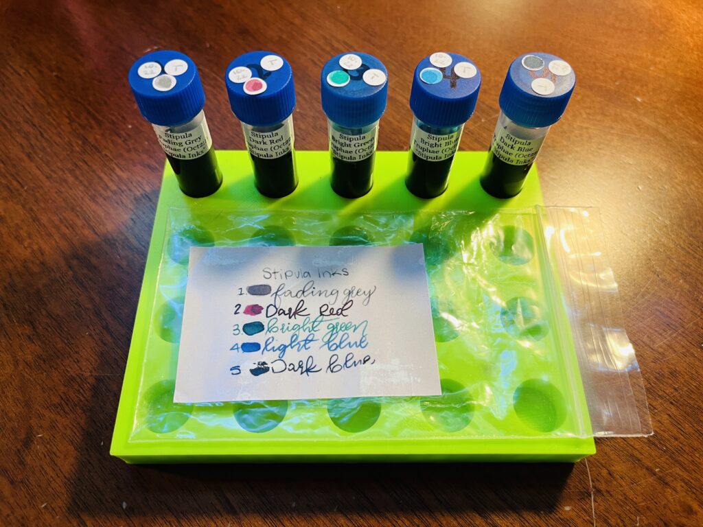 A lime green ink sample tray, 5 inks with the labeled plastic bag they arrived in. “Stipula, Fading Grey, Dark Red, Bright Green, Bright Blue, Dark Blue.