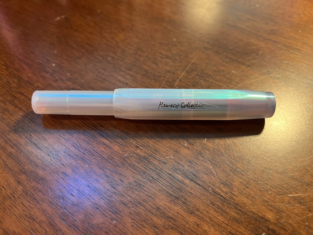 Kaweco Sport pen, sitting on a dark wooden desk top. The pen is an iridescent white. 