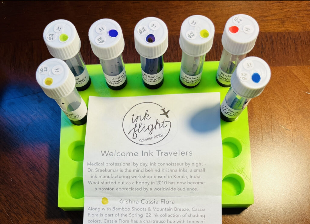 A lime green sample tray with 7 ink vials arranged in an upside down u around the edges of the Ink Flight note that comes with the pack. Text read “Ink Flight October 2022, Welcome Ink Travelers, Medical professional by day, ink connoisseur by night - Dr. Sreekumar is the mind behind Krishna Inks, a small ink manufacturing workshop based in Kerala, India. What started out as a hobby in 2010 has now become a passion appreciated by a worldwide audience.”