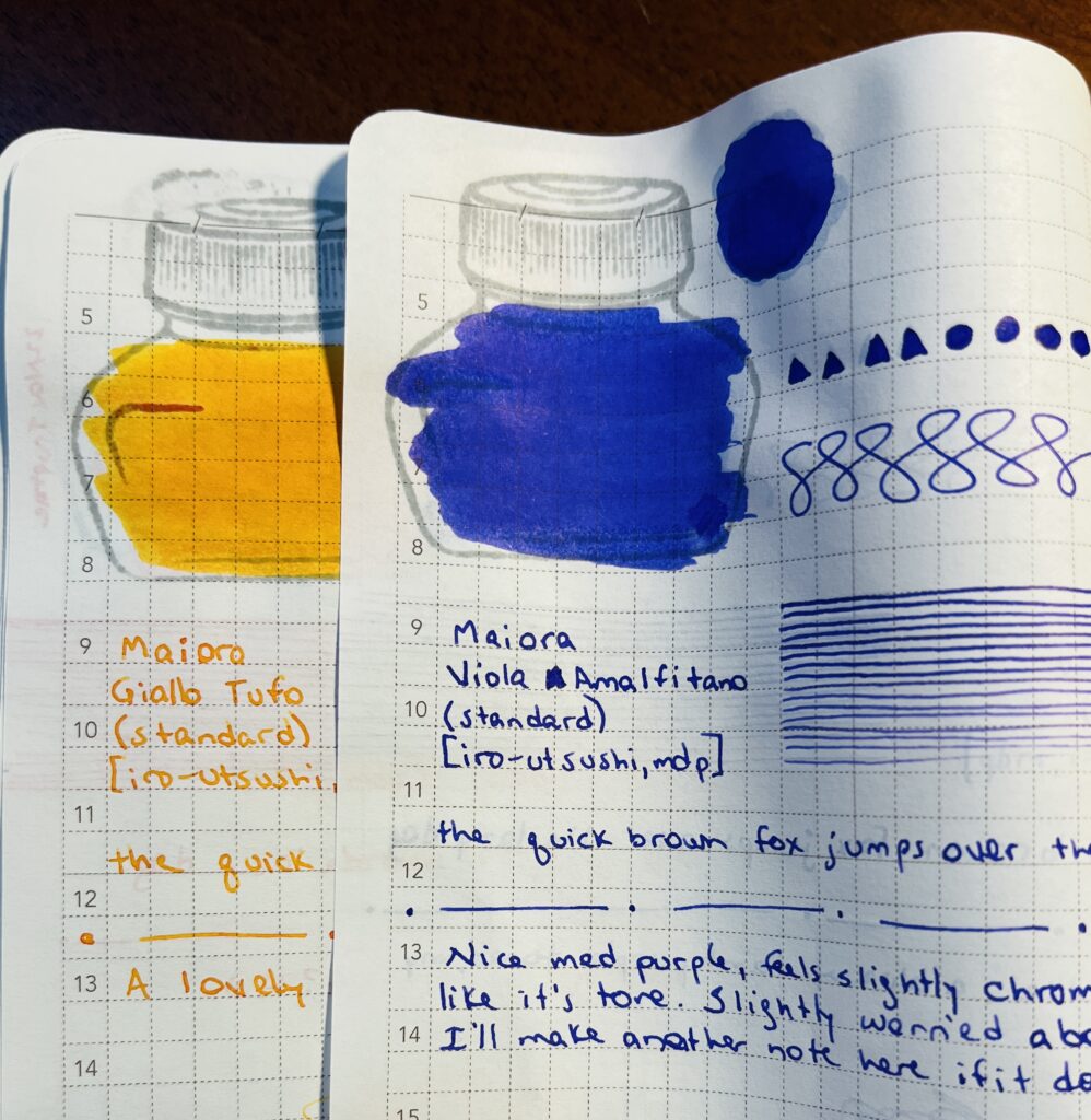 2 notebook pages overlapping each other, able to see just a portion of the bottom page, and more of the top page. There is a yellow and a blue ink sampled with shapes, swirls, straight lines, smudges and writing. 