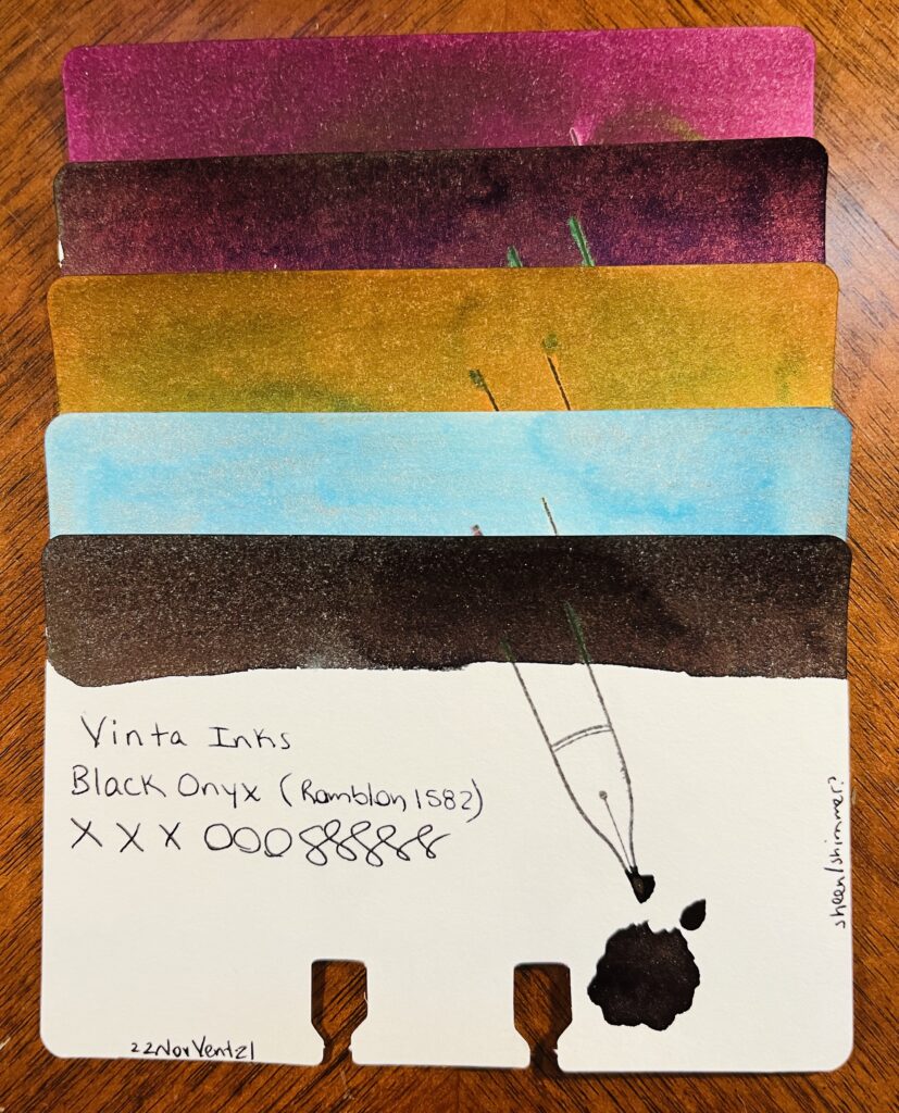 5 ink sample cards stacked on top of each other. Only the bottom one is visible, and you can see the ink swatch at the top, the name of the brand of ink, the name of the ink, xxxooosssssss, a stamp of a fountain pen nib, a pool of the ink, text at the bottom left reading “22NovVent-21” and on the right edge of the card is the text “standard.” From top to bottom there is a a light maroon, a darker maroon, gold, light blue, and a dark brown.