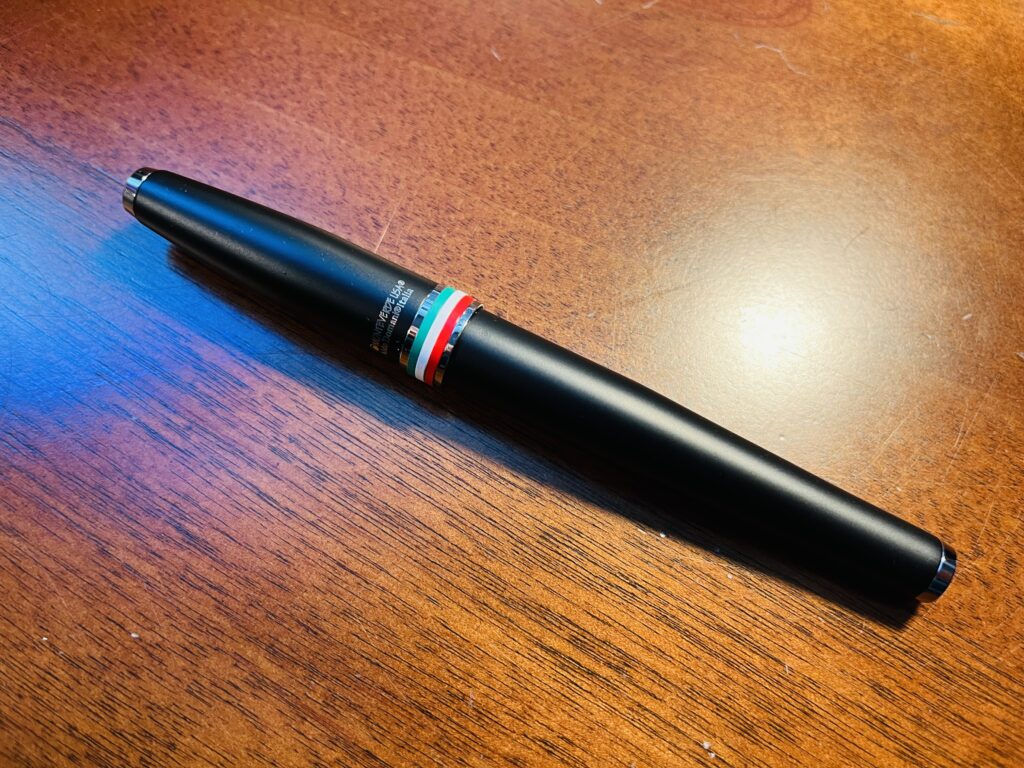 A black pen with small bands of around the bottom of the cap in green, white, and red. 