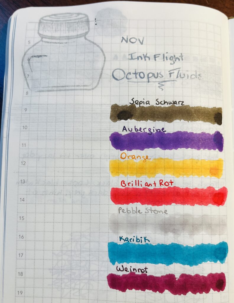A notebook page with the following text in silver: “Nov Ink Flight, Ocotopus Fluids” and then the name of each ink written in that inks color and then a line of the same color underneath. “Sepia Schwartz” is a brownish color, “Aubergine” is a gorgeous purple, “Orange” is a yellowish orange. “Brilliant Rot” is a super bright red, “Pebble Stone” is a light grey, “Karibik” is a teal, and “Weinrot” is a maroon. 