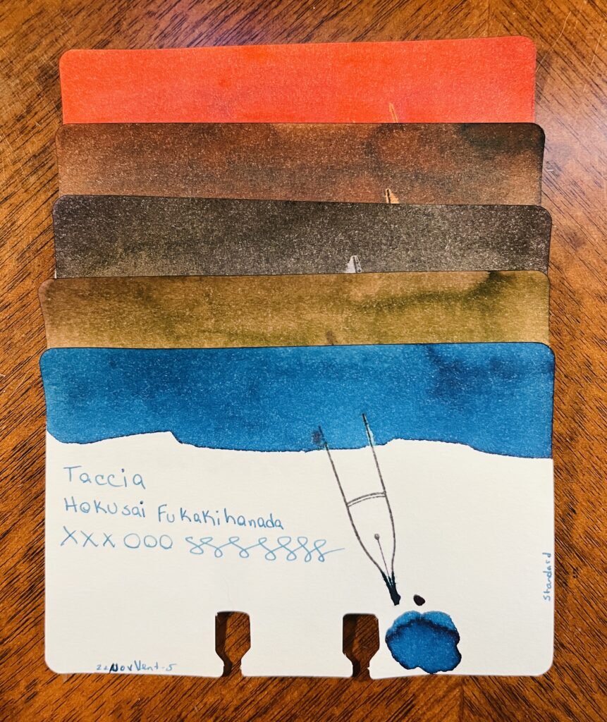 5 ink sample cards stacked on top of each other. Only the bottom one is visible, and you can see the ink swatch at the top, the name of the brand of ink, the name of the ink, xxxooosssssss, a stamp of a fountain pen nib, a pool of the ink, text at the bottom left reading “22NovVent-5” and on the right edge of the card is the text “standard.” From top to bottom there is a reddish ink, three various brown inks, and a blue ink. 