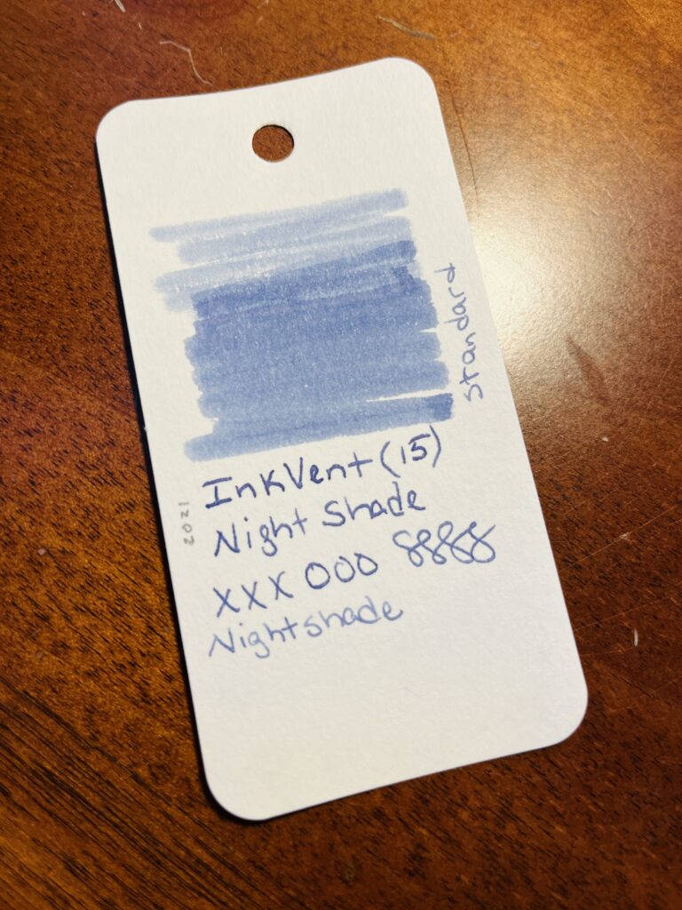 A sample card with a color swatch at the top, and the text says “Inkvent (15) Nightshade xxxooosss, standard, 2021” all of this is in an ink that looks like a light blue in this photo.