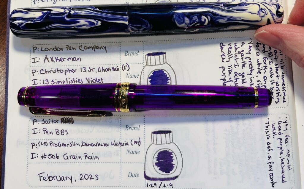 Two pens on a palette journal page. One is a slightly translucent warm purple with gold trim, and the other is a swirly cool purple mixed with white. 